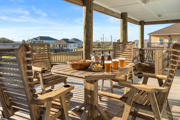 Covered wooden deck with dining table, Adirondack chairs, beers, snacks, and views of coastal homes and waterway